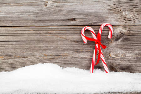 Colorful striped red and white Xmas candy canes with winter snow on wooden boards, with copyspaceの写真素材
