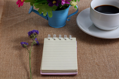 Cup of coffee on sackcloth floor with flowers and paper noteの写真素材