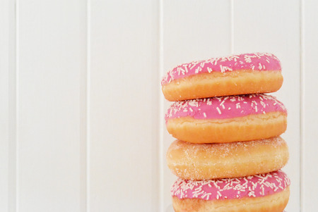 Stack of assorted pink donuts. White painted wooden planks on backgroundの写真素材