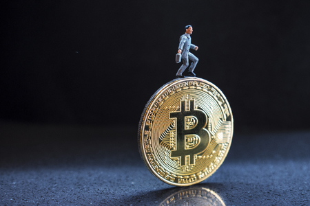 Side view of a miniature figure of businessman miner, standing on gold bitcoin. Dark background. Copy spaceの写真素材