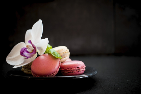Tender pink and cream macarons and flower on black stone background. soft focus, Place for your textの写真素材