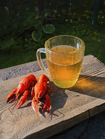 Glass of beer on a old wooden desk. Boiled crayfishes. Summer garden atmosphere.の写真素材