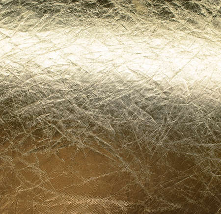Background of old crumpled gold foil, glossy textureの写真素材