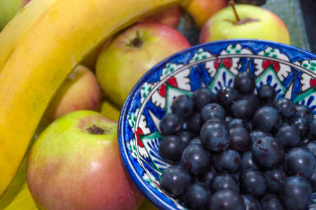Oriental bowl of black grapes with seasonal apples and bananaの写真素材