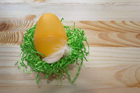 close up of yellow egg with white feather in artificial green nestの写真素材
