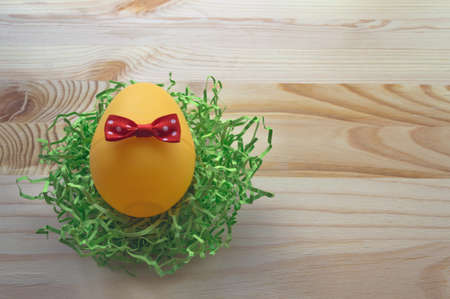 close up of egg decorated with red bow in nest on wooden backgroundの写真素材