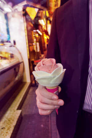 man holding rose ice cream in hand with blurred street on the background