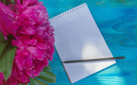 top view of notepad with pencil and bouquet of pink peony flowersの写真素材