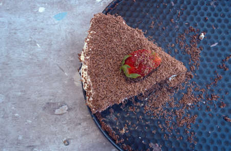 top view of piece of chocolate cake decorated with strawberry on grungy grey background