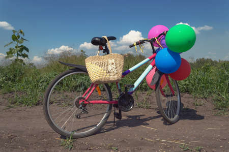 colorful bicycle decorated with balloons and straw bag on the rural road on sunny summer dayの写真素材