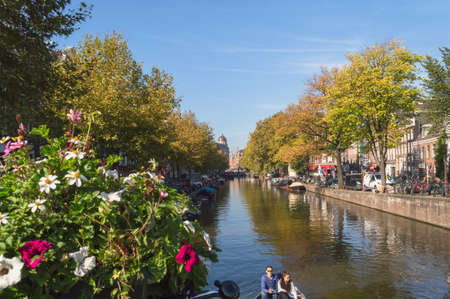 Amsterdam, The Netherlands, October 10, 2018: one of the central canals of Amsterdam with blurred flowers decorating bridge and couple sailing on boatのeditorial素材