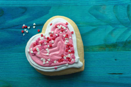 heart shaped cookie with valentines day pink decor and candy hearts on blue wooden background