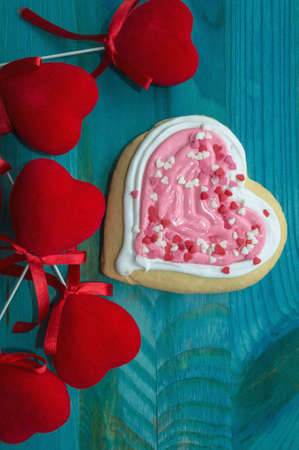 vertical image of heart shaped cookie and red velvet hearts decor on blue wooden background