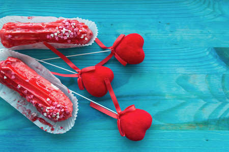 couple of red raspberry eclairs with red velvet hearts on blue wooden background with space for text