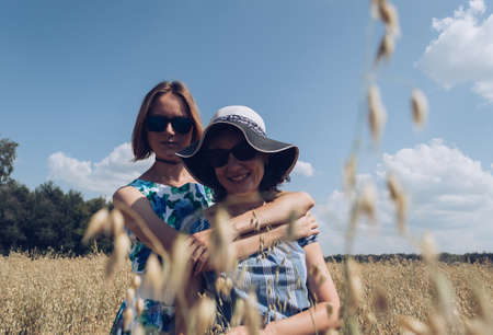 Retro styled  of hugging female friends standing in oat field on hot summer day