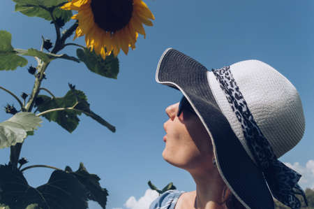 Profile of surprised young woman looking at tall blooming  sunflower