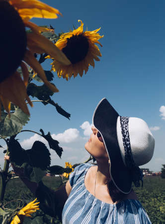 Vintage style  of young brunette woman in hat and sunglasses looking at blooming sunflowerの写真素材