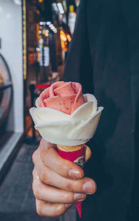 close up view of mans hand holding ice cream in rose shape at night market