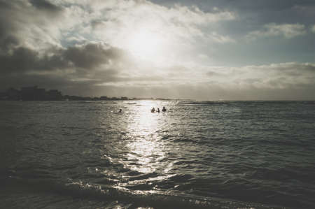 silhouettes of people standing in the sea at dusk with sparkling waterの写真素材