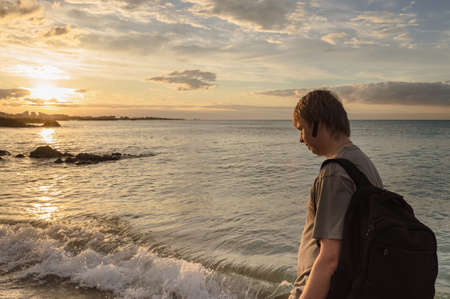 caucasian man with backpack is walking along the sea at Hamdeok Beach at sunsetの写真素材