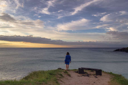 woman in blue dress standing at the edge of the hill near lava rock benchの写真素材