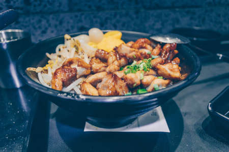 close up view of fried pork pieces over rice with bean sprouts and chopped green onion