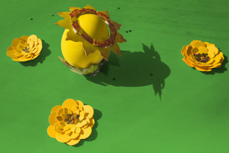 vivid Easter background of yellow egg and paper flowers in sunlightの写真素材