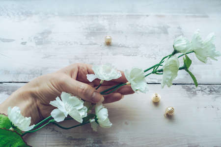 female hand tenderly holding branch of white blooming artificial  flowers with beads on wooden backgroundの写真素材