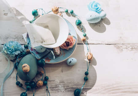 top view of porcelain tea set with tea bag inside blue wooden egg flowers beads and ribbonsの写真素材