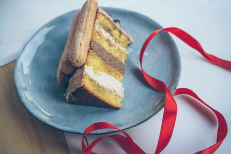 slice of tiramisu cake lying on plate  with red ribbon decor