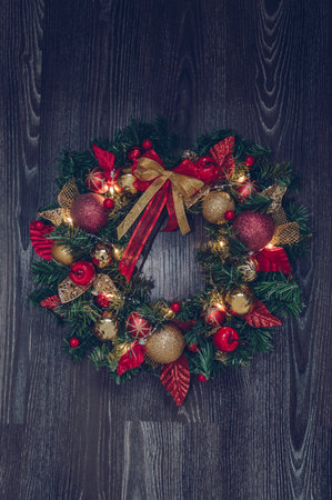 illuminated handmade christmas wreath on dark wooden background with red and golden decorの写真素材