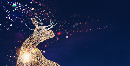 template for winter holidays with illuminated reindeer sculpture sparks and lights on daek night backgroundの写真素材