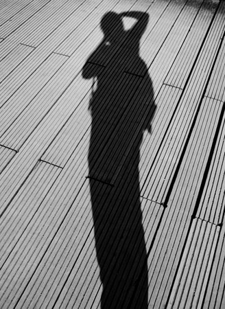 Shadow of a woman standing on a wooden pier. Black and white photo.の写真素材