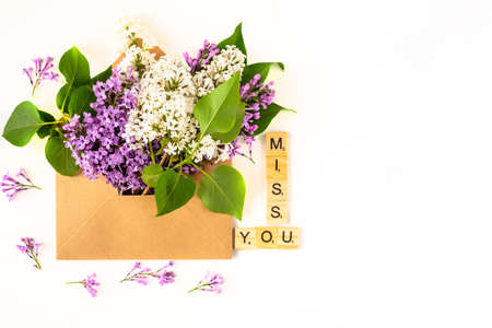 Close up of opened craft paper envelope filled with spring blossom purple lilac flowers laying on white background. Top view. Concept of love and missing someone.の写真素材