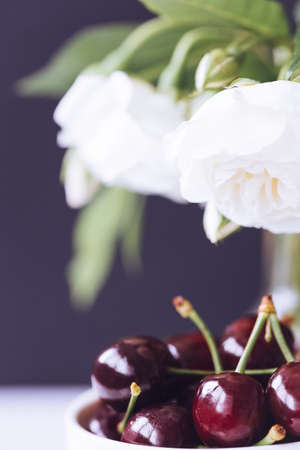 Fresh ripe cherries in ceramic bowl and white roses. Close up. Healthy and romantic breakfast concept. Summer wedding decoration idea.の写真素材