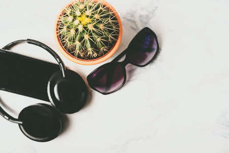 Flat lay, top view of cactus, mobile phone, sun glasses and audio headphones over marbe background with copy space. Minimalist style. Minimal hipster concept.の写真素材
