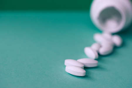 Pills spilling out of bottle on pastel blue paper background with copy space in minimal style,...