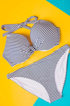 Top view of two pieces striped blue and white swimming suit on blue and yellow pastel background. Copy space. Concept of vacation.の写真素材
