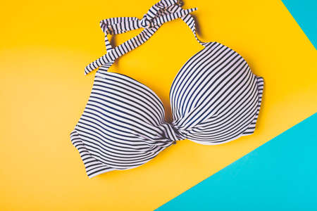 Top view of striped blue and white swimming bra on blue and yellow pastel background. Copy space. Concept of vacation.の写真素材