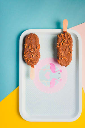 Dessert chocolate ice cream bars with nuts, wooden stick on blue and yellow pastel background....