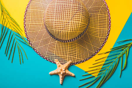 Summer composition. Tropical palm leaves, straw beach hat, starfish on pastel blue and yellow background. Concept summer trip. Flat lay, top view, copy space.の写真素材