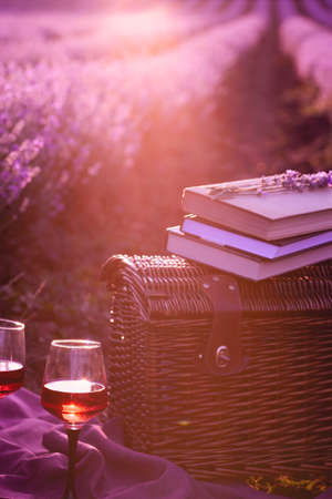 Picnic basket, old books, glasses wine under the rays of the setting sun. Romantic picnic concept at sunset in a fragrant lavender field.の写真素材
