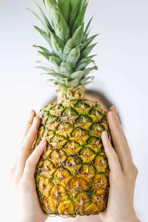 Girl holding a pineapple in front of her face over white background. Raw eating concept Summer and vacantion time.の写真素材
