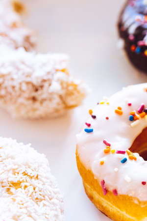 Assorted multicolored donuts in a bakery box with chocolate frosted, glazed and sprinkles donuts. Sugar addiction or festive menu concept.の写真素材