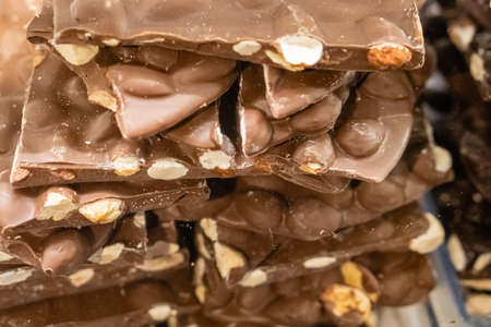 Closeup stack of assortment luxury handmade milk chocolate bars with nuts in shop window. Selective...