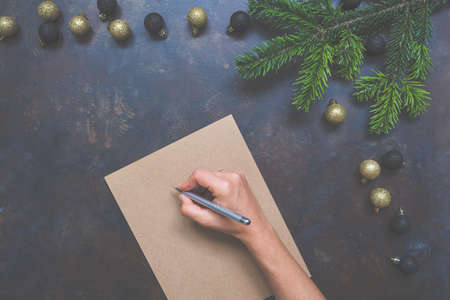 Woman writing Christmas letter or New Year goals on paper on dark vintage background with decorations, top view, copy space. Mock up for to do plans, ideas and hand lettering compositions.の写真素材