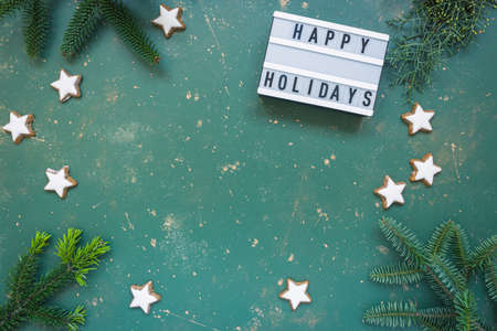 Christmas composition, frame made of conifer branches, different winter plants, light box with text Happy holidays and cookies on green vintage background. Flat lay, top view, copy space.の写真素材