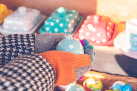 Gloved hands of woman holding a ceramic Christmas toy with dots on the street seasonal market.