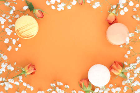 Colourful french macaroons or macarons on pastel orange background. Floral frame.の写真素材