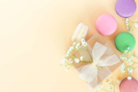 Present box with ribbon and colorful macarons, macaroons on beige background. Celebration, birthday event. Flat lay, top view, copy space.の写真素材